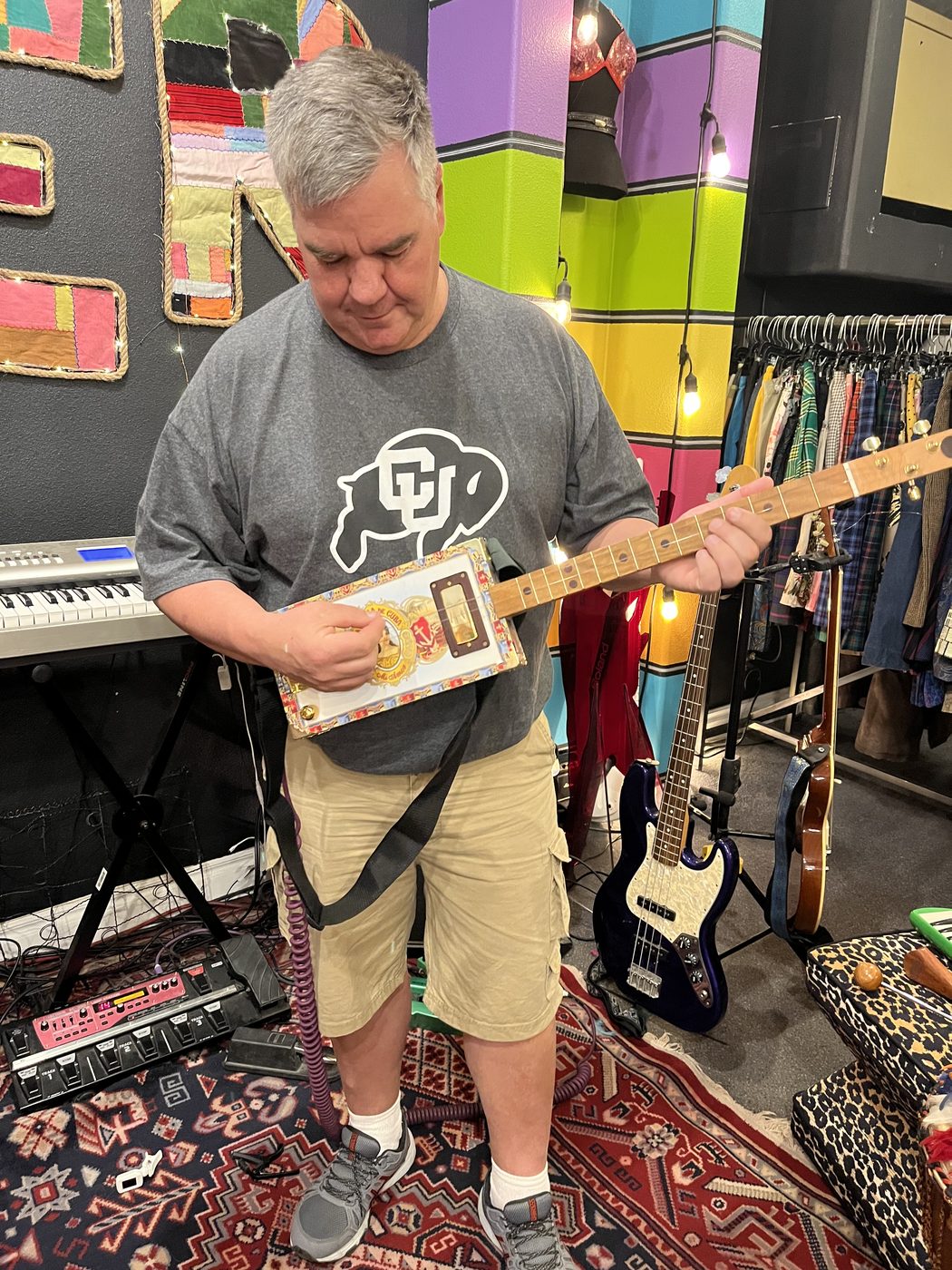 Toby Leonard playing a handmade cigar-box guitar in a brightly painted shop full of instruments